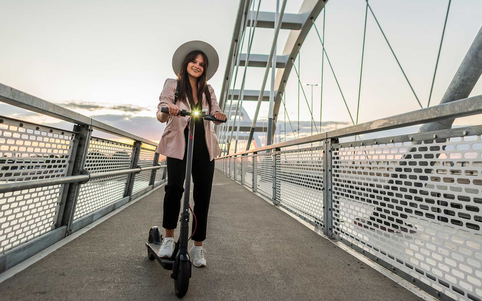 Eine lächelnde junge Frau steht auf einem E-Scooter auf einer Brücke