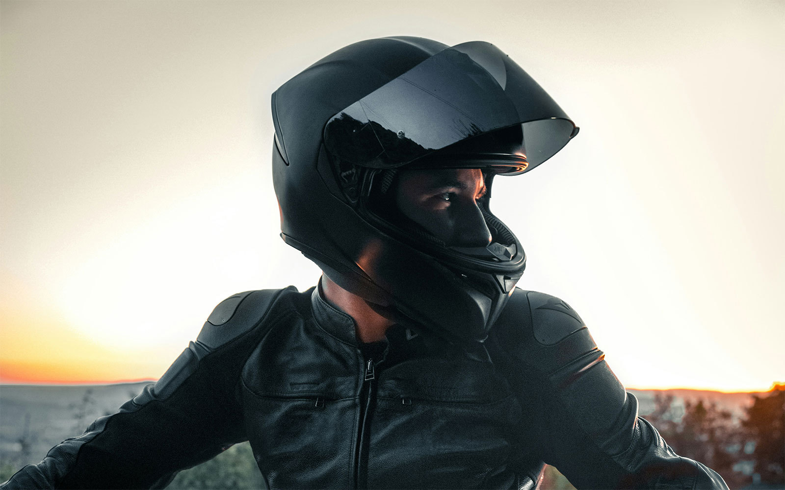 Ein Motorradfahrer in einer schwarzen Lederkombi blickt aus seinem Helm