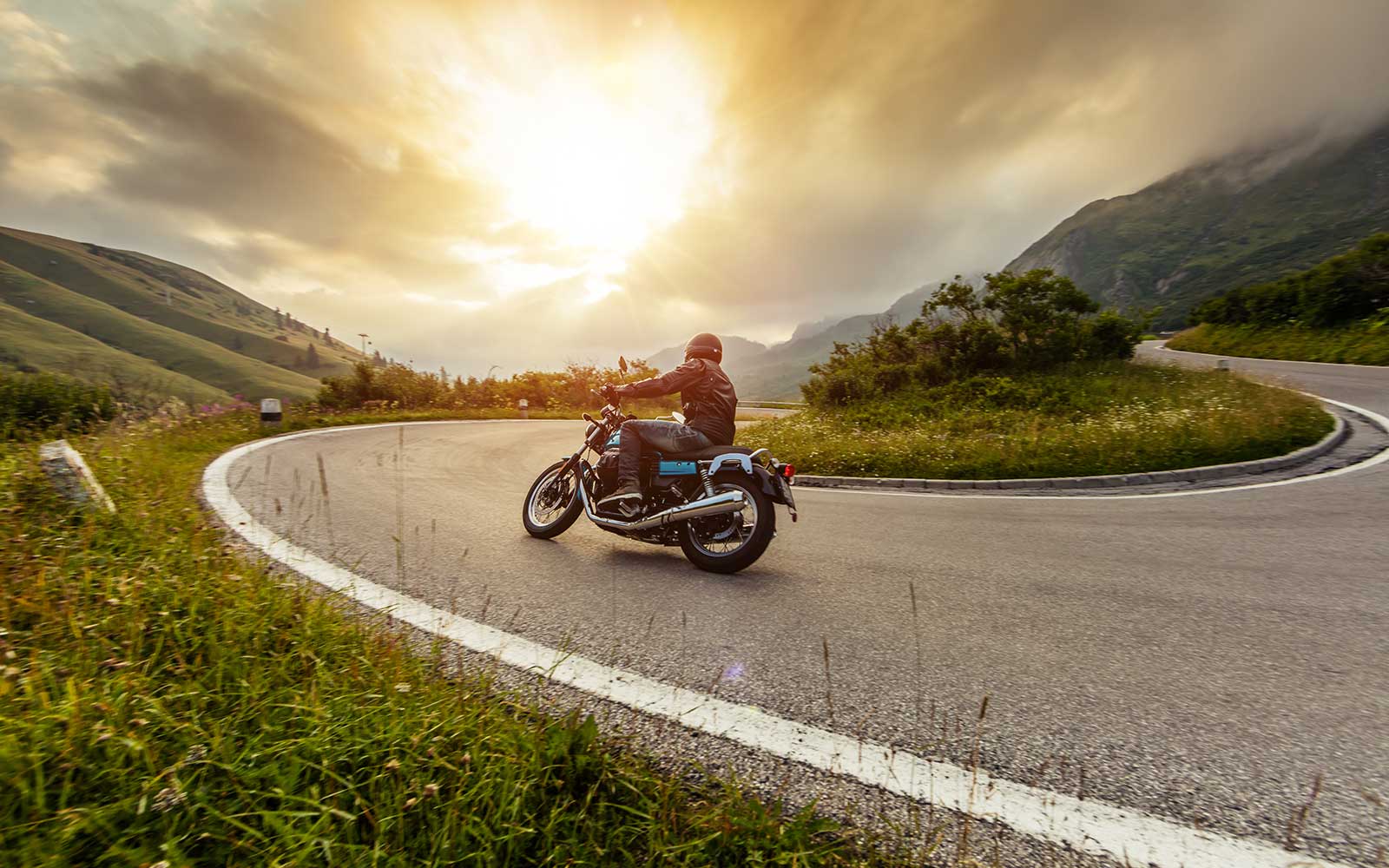 Ein Motorradfahrer fährt mit einem alten Motorrad eine Passstraße im Gebirge