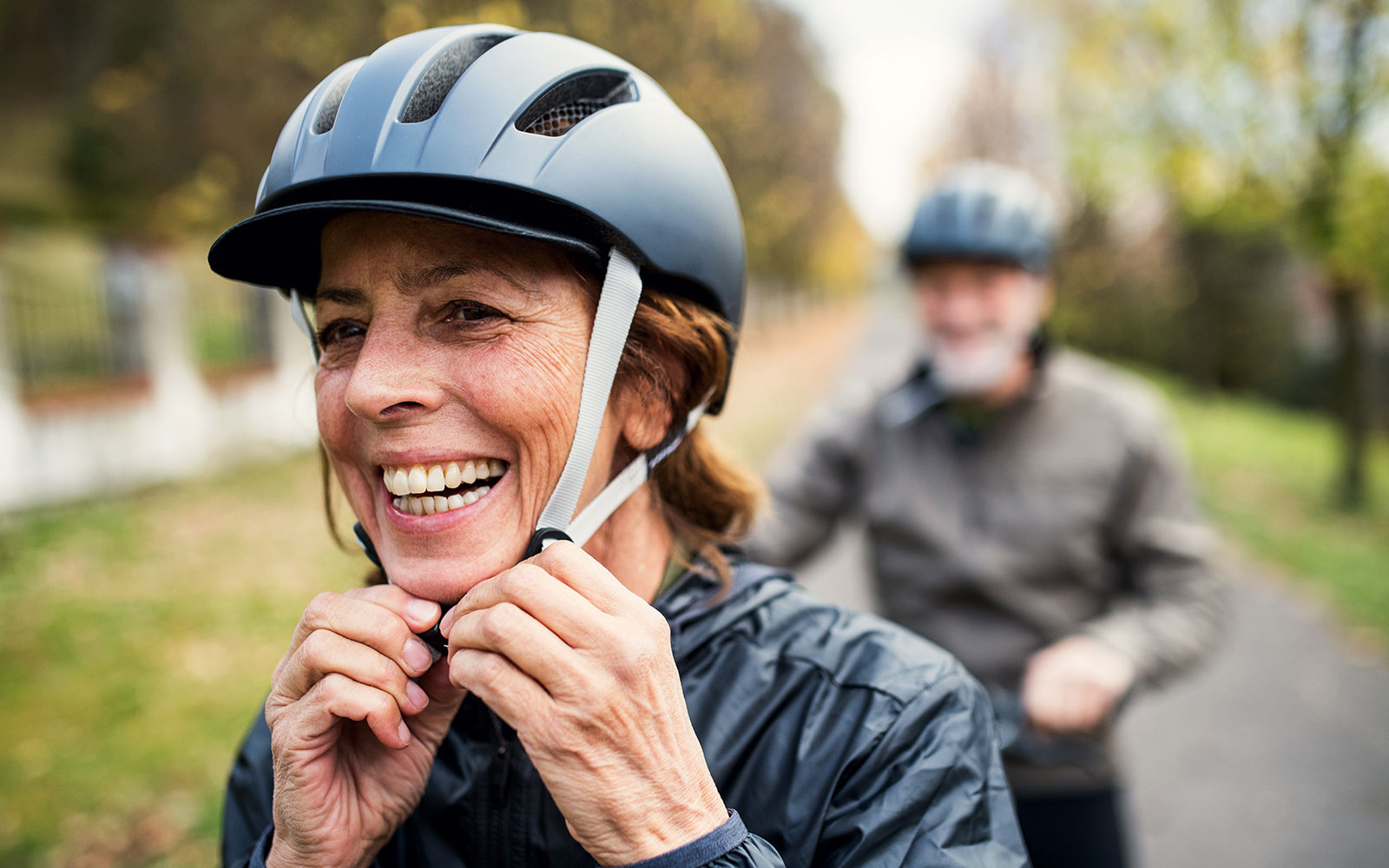 Eine ältere Dame setzt sich einen schwarzen Helm auf, um mit dem E-Bike los zu fahren