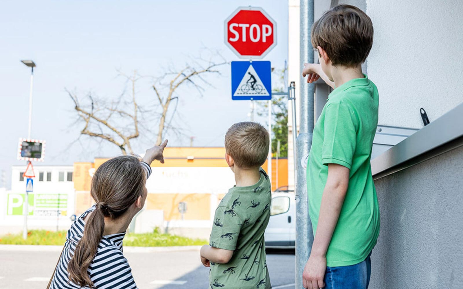 Eine Frau zeigt zwei jungen Burschen das Stopp-Schild an einer Verkehrskreuzung.