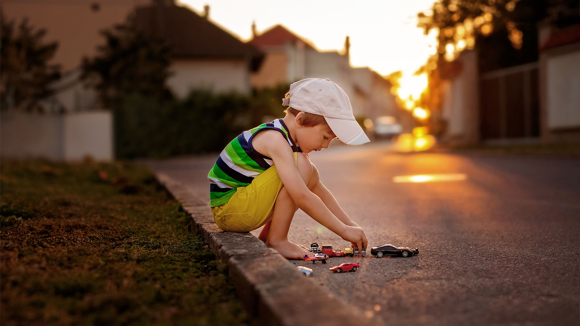 Ein kleiner Junge spielt mit seinen Spielzeugautos in seiner eigenen Welt auf der Straße und vergisst darauf im Straßenverkehr zu sein.