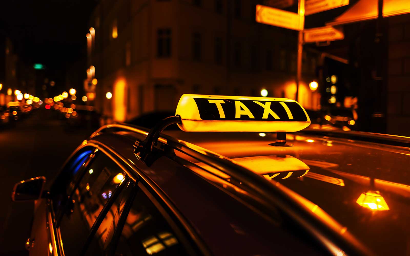 Ein beleuchtetes Taxischild auf einem fahrenden Taxi in der Nacht.