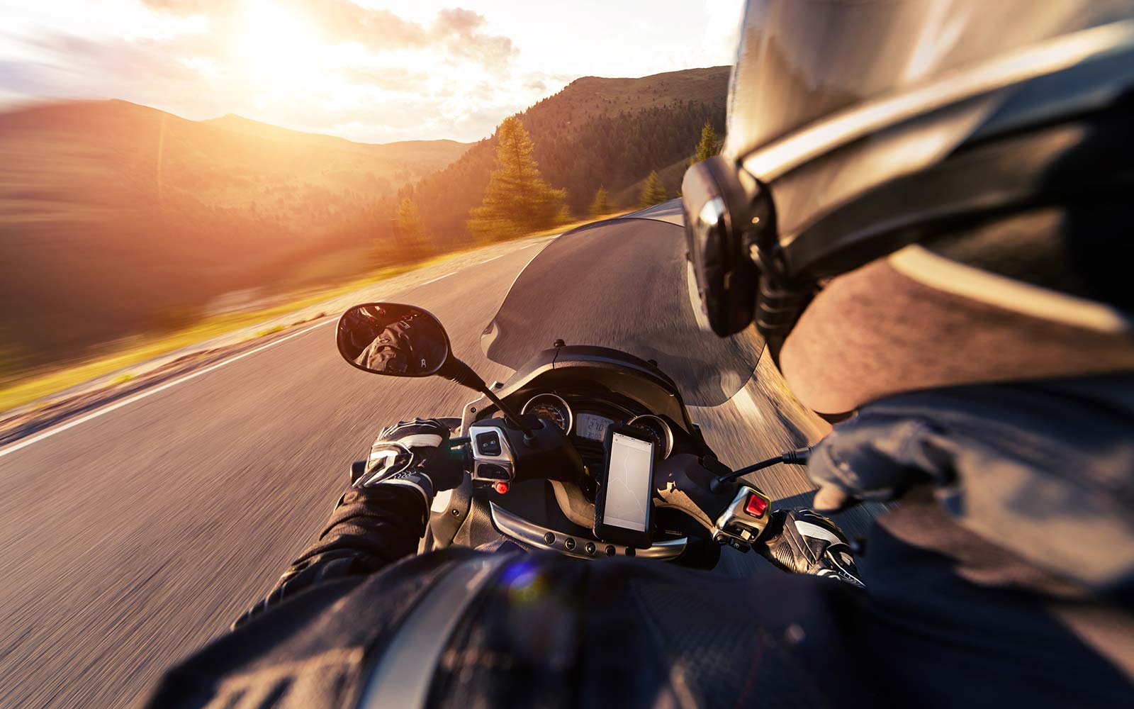 Ein Motorradfahrer fährt bei gegenlichtigem Sonnelicht um die Kurve.